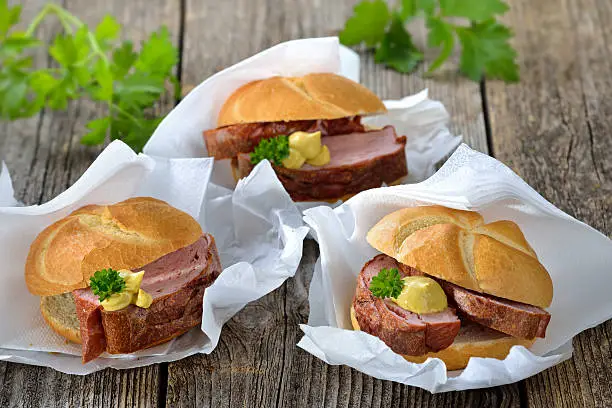 Bavarian takeaway food: Three rolls with baked meat loaf and mustard on wrapping paper with a napkin