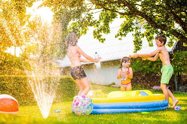 мальчик плещущиеся девочек с водяной пистолет в саду - water toy стоковые фото и изображения