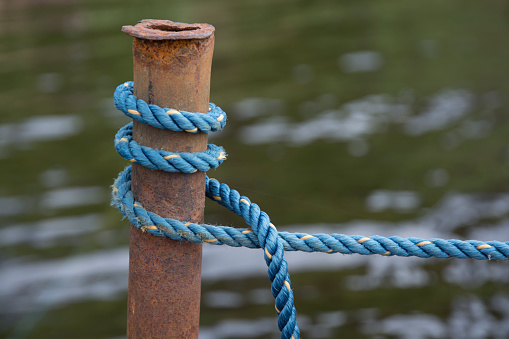 Blue boating knot rope tied around rusty pole by the water.