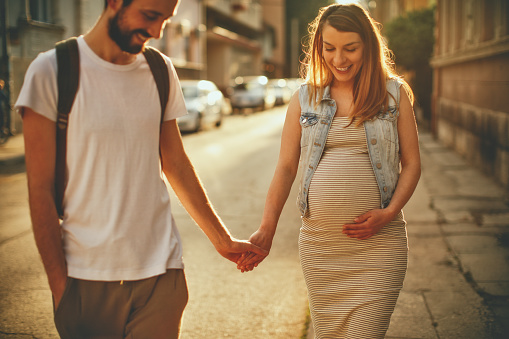 Photo of a young couple, soon to become parents, enjoy their walk on a beautiful sunny day