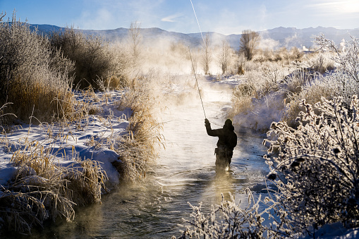 Fly Fishing in Extreme Cold Winter Conditions - Scenic winter landscape with fly fisherman recreating on cold trout mountain stream.  Colorado, USA.
