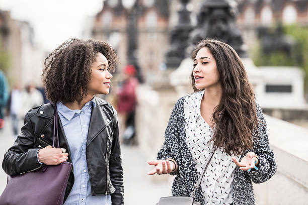 Two female friends talking outdoors in Paris, France Two young women walking in Paris street having conversation. Young woman gesturing with hands, female friend listening street friends stock pictures, royalty-free photos & images