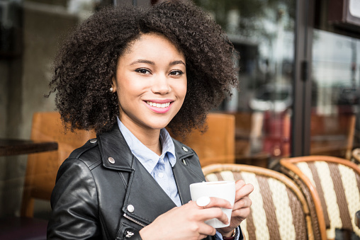 Portrait of attractive young woman holding coffee cup in cafe, looking at camera. Happy young woman relaxing in cafe