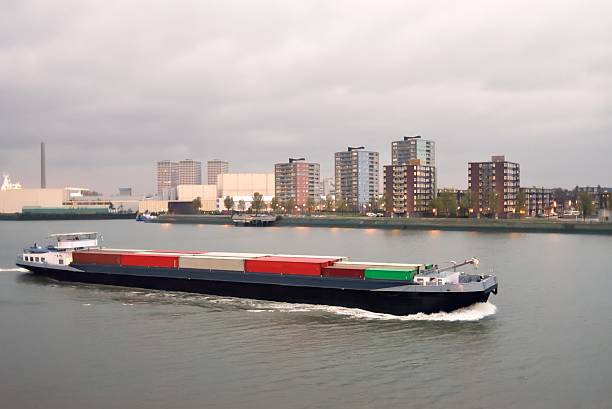 A barge with containers glides by on a cloudy, rainy morning in the New Waterway of Rotterdam with apartment buildings in the background