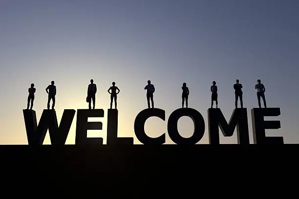 Group of people standing on the word welcome at sunset creating a silhouette.