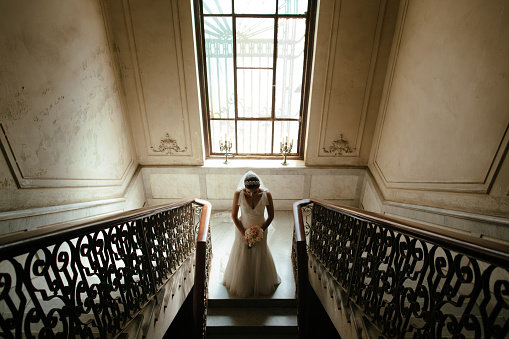 A beautiful Hispanic bride standing in front of a stairway and a home in Havana Cuba in this horizontal shot.