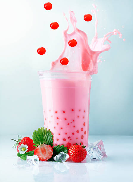 Fruity pink strawberry boba tea splashing from a glass with falling red tapioca pearls, ice and ripe delicious strawberries