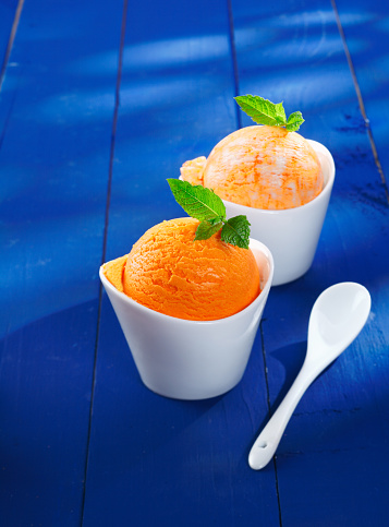 Tangy orange Italian icecream in individual white boat-shaped bowls served on blue painted wooden boards with copyspace