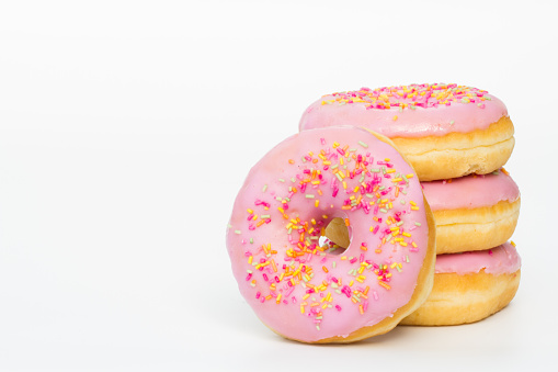 A stack of donuts covered with pink icing and sprinkles on an isolated white background.