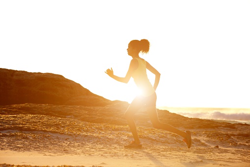 Full length side portrait of a female runner with sunset