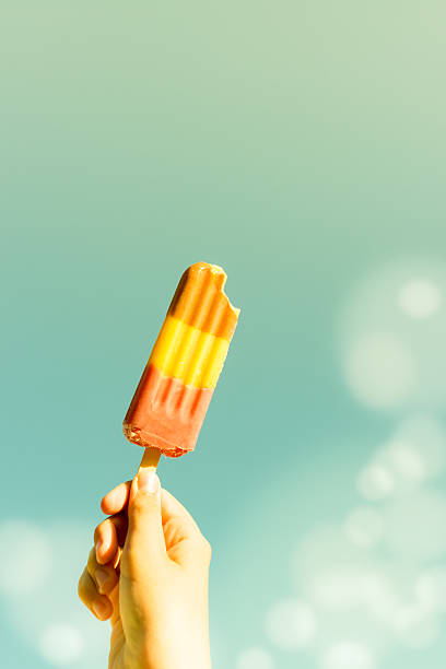 Hand holding a lollipop ice against the clear sky