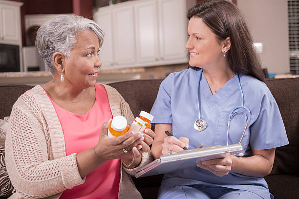 Home healthcare nurse discussing medications to senior adult woman. Caring, Latin descent home healthcare nurse discusses prescription medications with African descent senior adult patient at home, assisted living, or nursing home setting.  She holds a clipboard as she explains the medication information.  Kitchen background. pill bottle photos stock pictures, royalty-free photos & images