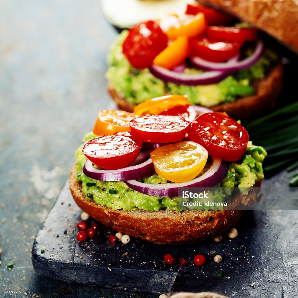 Tasty homemade sandwiches with avocado, tomato, onion and pepper Tasty homemade sandwiches with avocado, tomato, onion and pepper on a slate board Appetizer Stock Photo