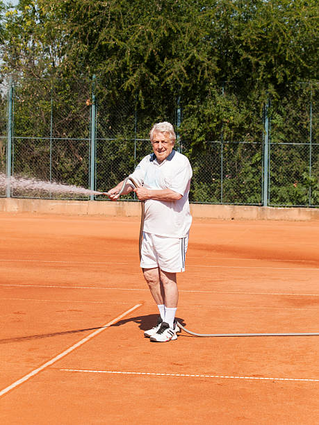 istock Old men sprinkling tennis court before playing 531974714