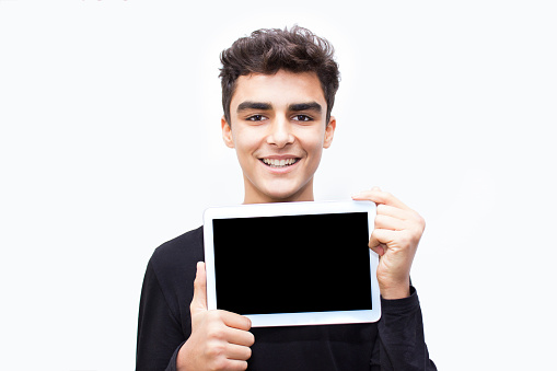 Portrait of smiling young man showing empty digital tablet. There is copy space for your text or image on digital tablet's screen. Laughing teenage boy looking at camera in happiness. Horizontal composiiton. Studio shot.