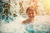 Little girl playing in waterfall in waterpark swimming pool