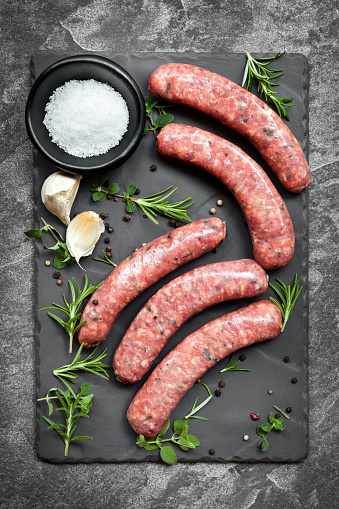 Raw sausages on slate, with herbs and spices.  Overhead view.