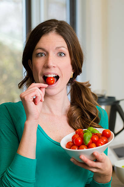 Young woman showing a cherry tomatoes in your mouth