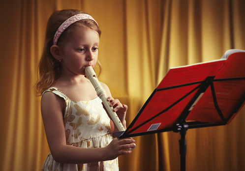 Little skillful girl playing flute with sheet of music