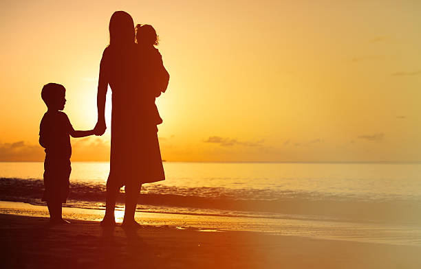istock mother and two kids walking on beach at sunset 531993850