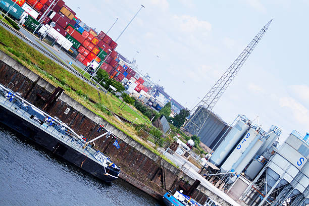 Duisburg, Germany - July 12, 2014: Freight ships are anchore at pier in inland harbor Duisburg. On pier are tanks, In background are many stacked containers. Summer shot at Ruhr,