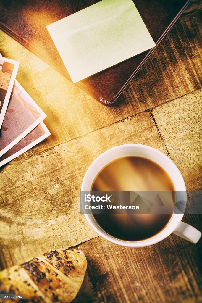 Lens flare and coffe on table top A cup of coffee placed on a rustic wooden table with a croissant. Photographic filters help making a warm and cozy mood. There is left space on the note-paper to individual text 2000-2009 Stock Photo