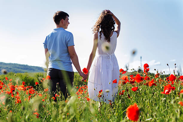 joven feliz pareja en un prado de poppies completo - cut flowers women field single flower fotografías e imágenes de stock