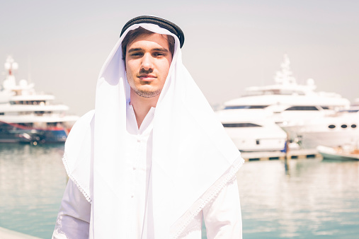 young arabian man standing next to a yacht port