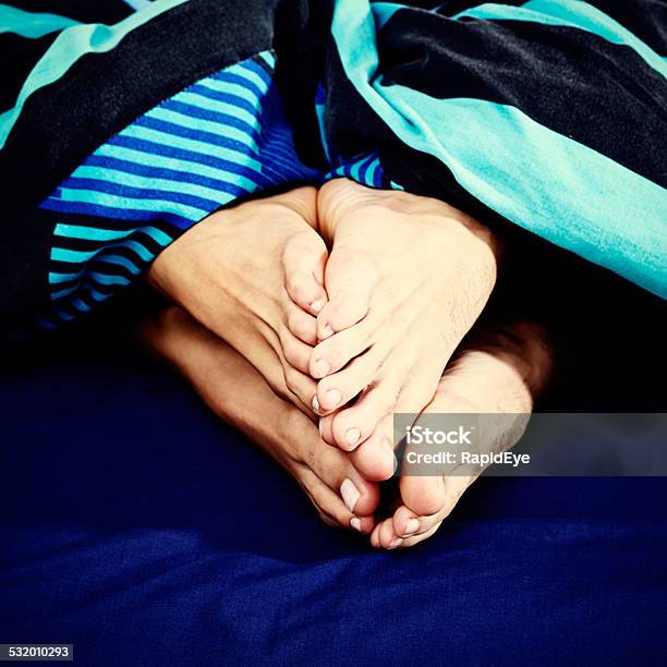 Soletosole Two Pairs Of Feet Touch Affectionately Under Duvet Stock Photo - Download Image Now