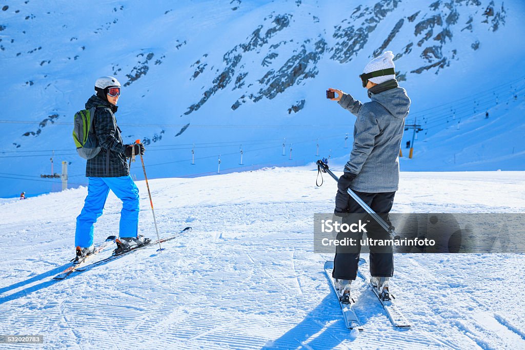 Photographing  Snow skier   Skiing couple  Teens boy and girl enjoying Photographing, Snow skier - Skiing couple. The girl photographed boyfriend. Teens boy and girl enjoying in the sun, snow and winter vacation. Shot with Canon 5DMarkIII, developed from RAW, Adobe RGB color profile. Skiing Stock Photo