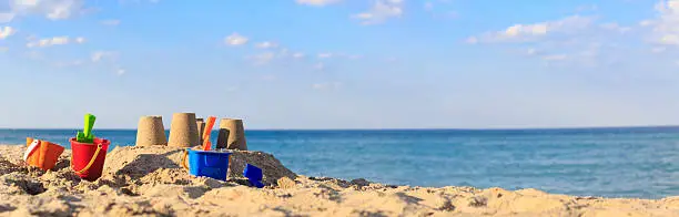 Sand castle on the beach with toys, wide panorama