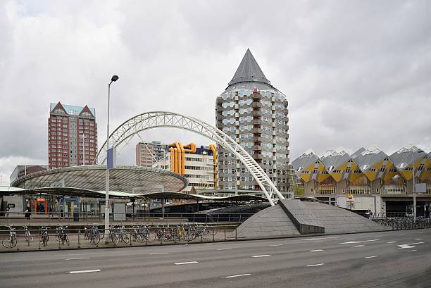 This is the Rotterdam Blaak metro station with its ticket kiosk and incidental commuters and tons of the ever present bicycles and two modern high rise apartment buildings. Also the exposed orange pipes lend a bit of color on this dreary day.