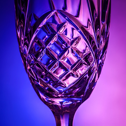 A close-up, silhouette of a wine glass on a blue and purple background