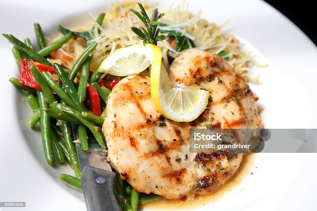 Lemon Rosemary Chicken On Plate Of Spaghetti And Green Beans A restaurant style plate of lemon rosemary chicken on a bed of steamed green beans and thin spaghetti topped with a lemon twist. Chicken Meat Stock Photo