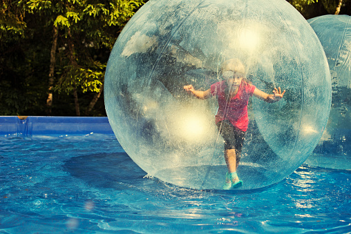 Little girl having fun in amusement park inside a giant inflatable water sphere. Sunny summer day.