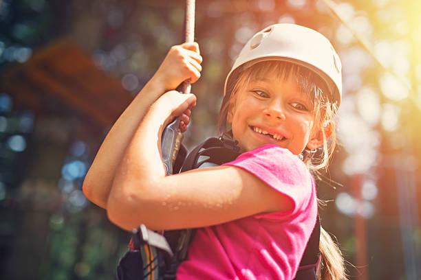 Little girl zipping in zip line adventure park Little girl wearing a helmet, on zip line in adventure park. The girl is aged 7 and is laughing. canopy tour photos stock pictures, royalty-free photos & images