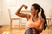 Happy athletic woman flexing her bicep at home.
