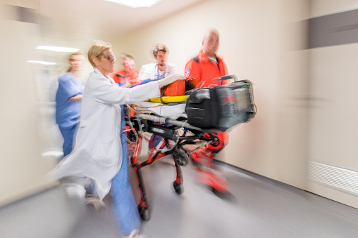 Paramedics, doctor and nurse wheeling patient on stretcher in hospital corridor.