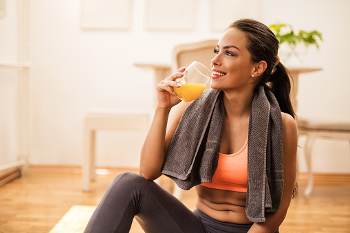 Young smiling athletic woman relaxing after exercising and drinking orange juice.