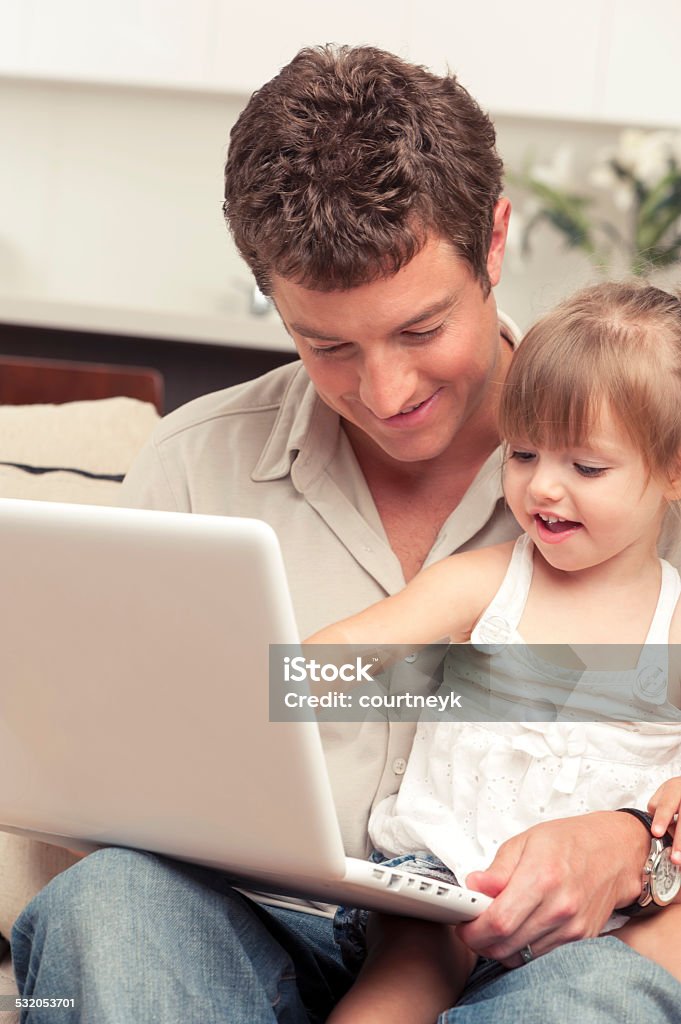 Father with daughter relaxing on the couch using laptop Father with daughter relaxing on the couch using laptop at home in the living room. The little girl is having fun and pointing to the screen of the computer. 2015 Stock Photo