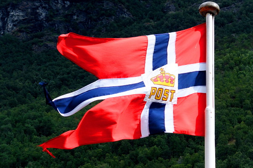 Norwegian flag on Fjord1 boat with trees in the background, Flam