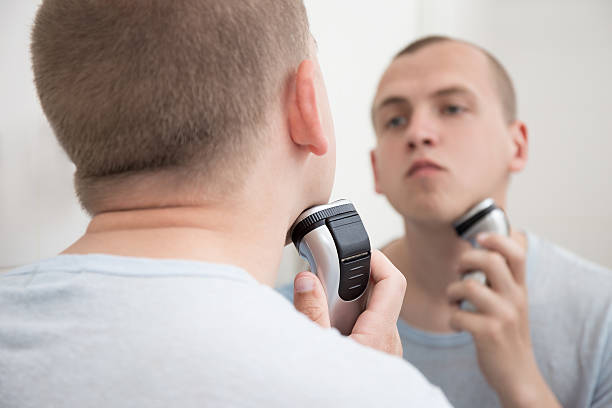 istock young man in mirror shaving with electric shaver 532058740
