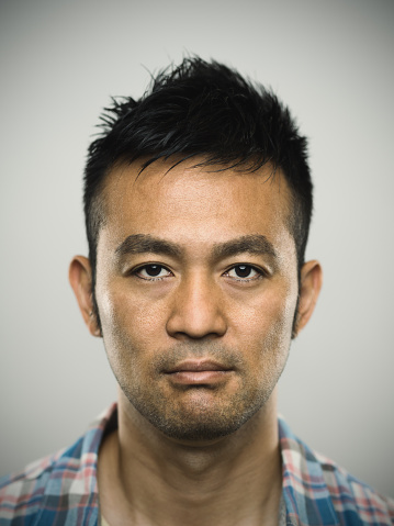 Studio portrait of a japanese young man looking to the side with relaxed expression and fresh smile. The man has around 35 years and has short hair and casual clothes. Vertical color image from a medium format digital camera. Sharp focus on eyes.