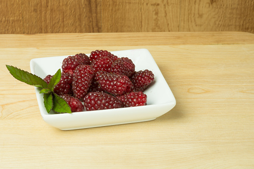Tayberries and mint on white plate on wooden table