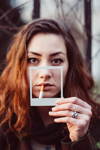 Young girl showing instant selfie of mouth with cigarette and premature skin aging process