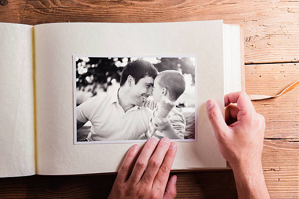 Fathers day composition. Photo album, black-and-white pictures. Fathers day composition. Hands of unrecognizable man holding a photo album, black-and-white pictures. Studio shot on wooden background. photo album photos stock pictures, royalty-free photos & images