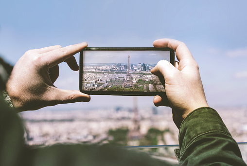 Cropped image of man photographing Eiffel Tower. Male is taking picture of monument through smart phone. He is visiting one of the most famous place in Paris.