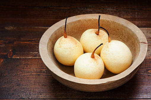 Fresh ripe organic pears in a wooden bowl on a rustic wooden table, selective focus