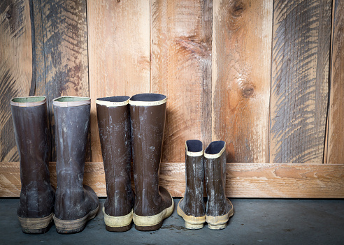 Large and small brown rubber boots sitting next to a wooden barn door.
