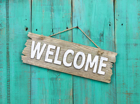 Wood welcome sign hanging on rustic turquoise wooden fence